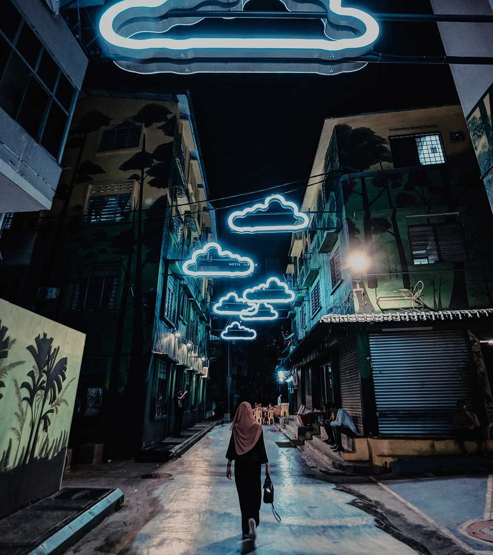 Woman walking along a dark city street with neon cloud signs above her
