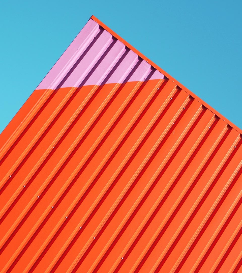 Brightly painted abstract view of a shipping container against a mid-blue sky