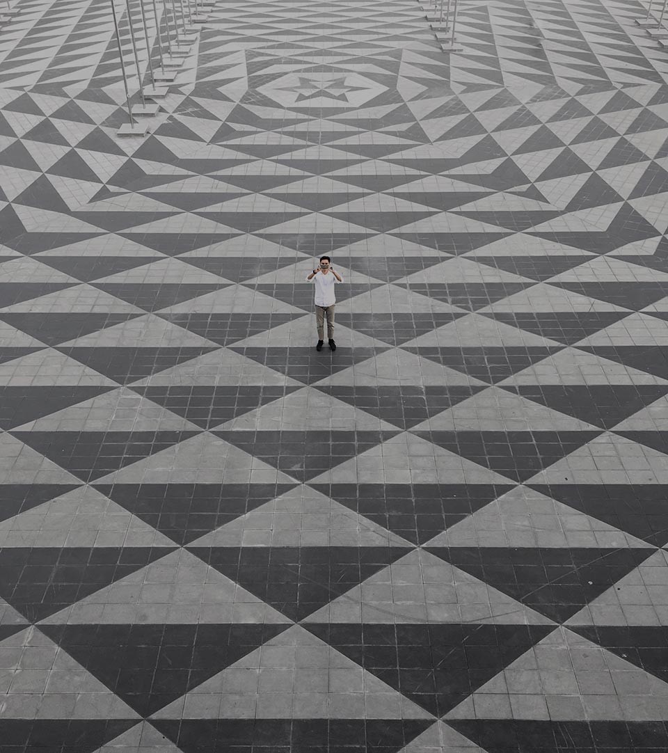 Individual standing on geometric two-tone grey paving. Image taken from above